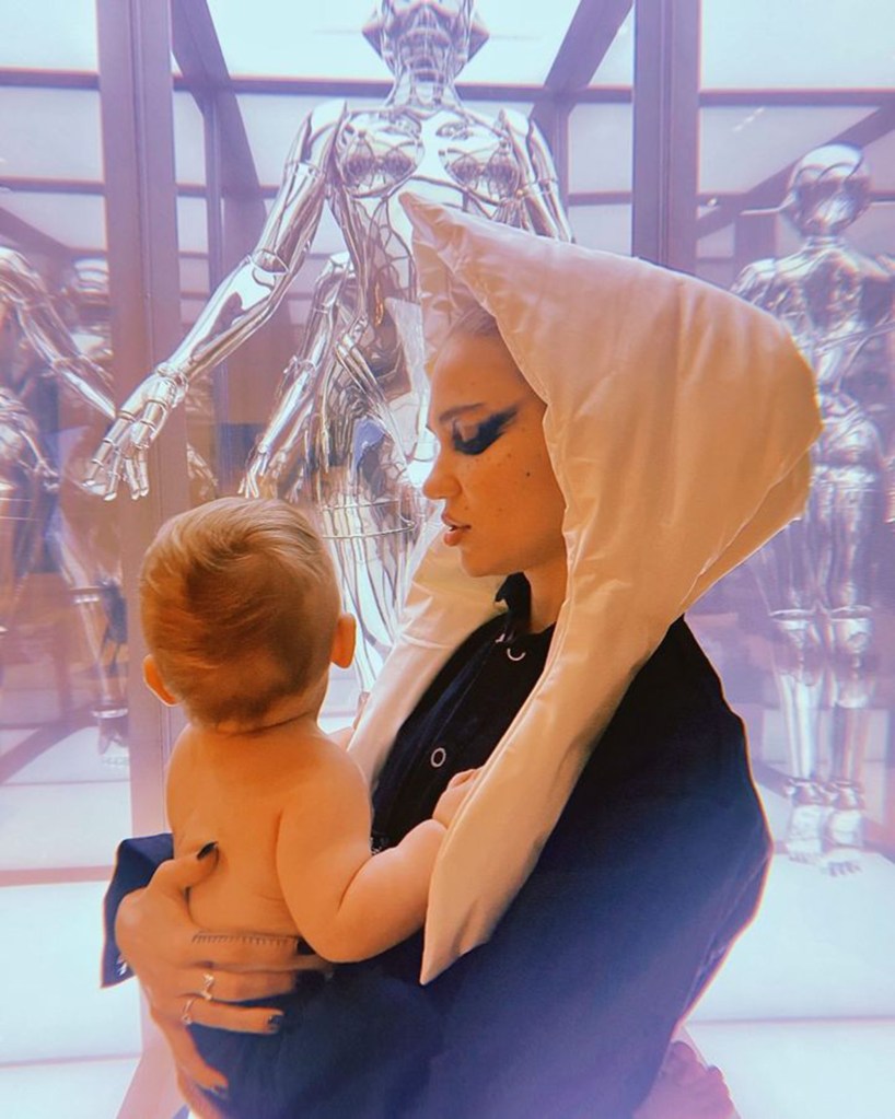 Grimes holds her baby, Exa Dark Sideræl, in front of a glass display of metallic figures.