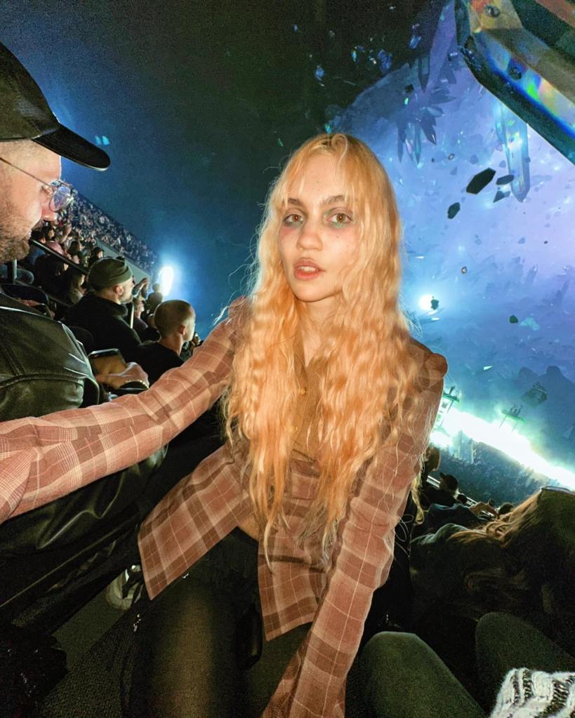 Grimes with long blonde hair, wearing a plaid shirt, at an event.