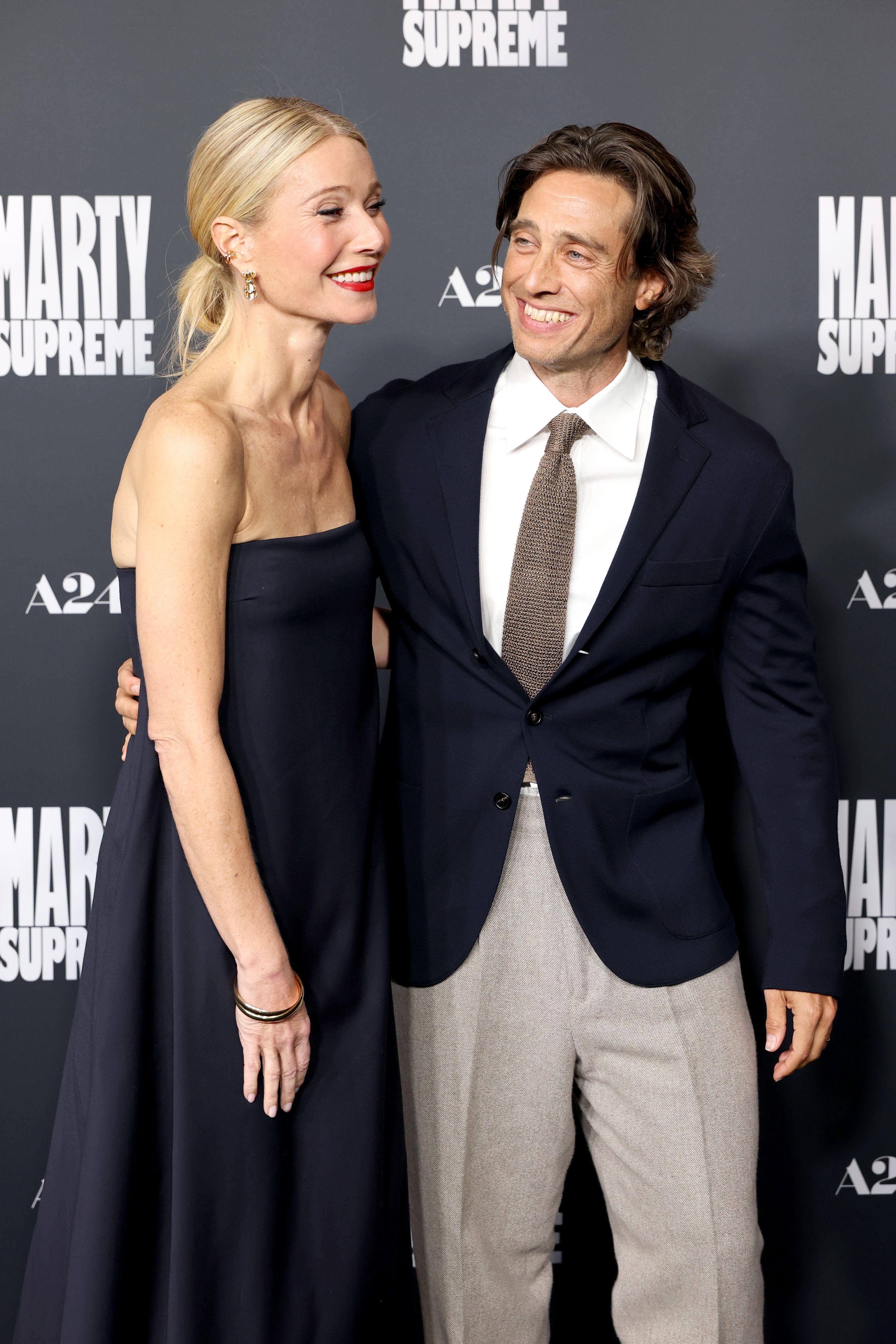 Gwyneth Paltrow in a dark strapless gown and Brad Falchuk in a dark blazer and light pants posing at the Los Angeles premiere of
