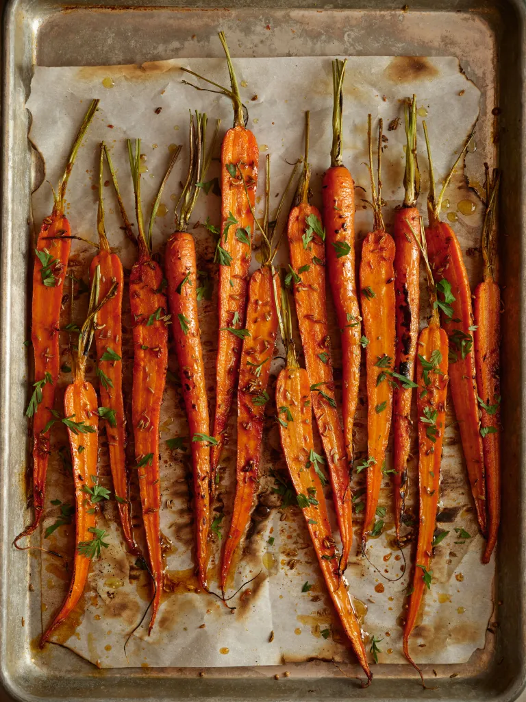 Roasted carrots with herbs and seasoning on a baking sheet.