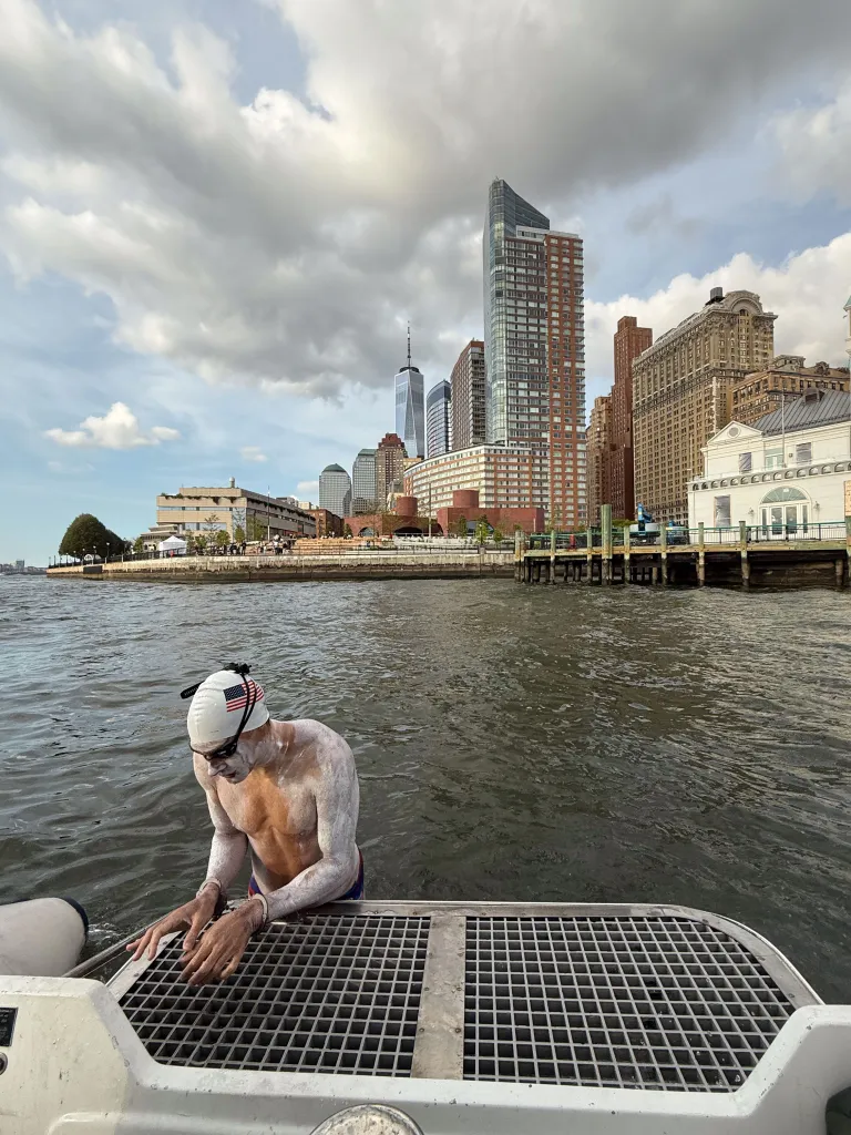 Michael Moreau hanging on the back of a boat. Lower Manhattan in the background