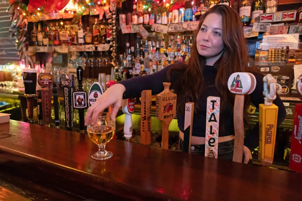 Hannah Teal at George & Jack's Tavern in Williamsburg, Brooklyn, behind a bar with various beer taps.