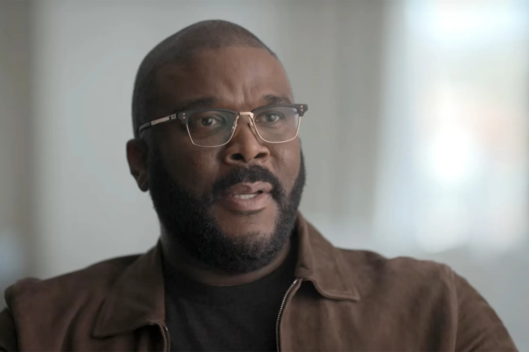 Tyler Perry wearing glasses and a brown jacket.