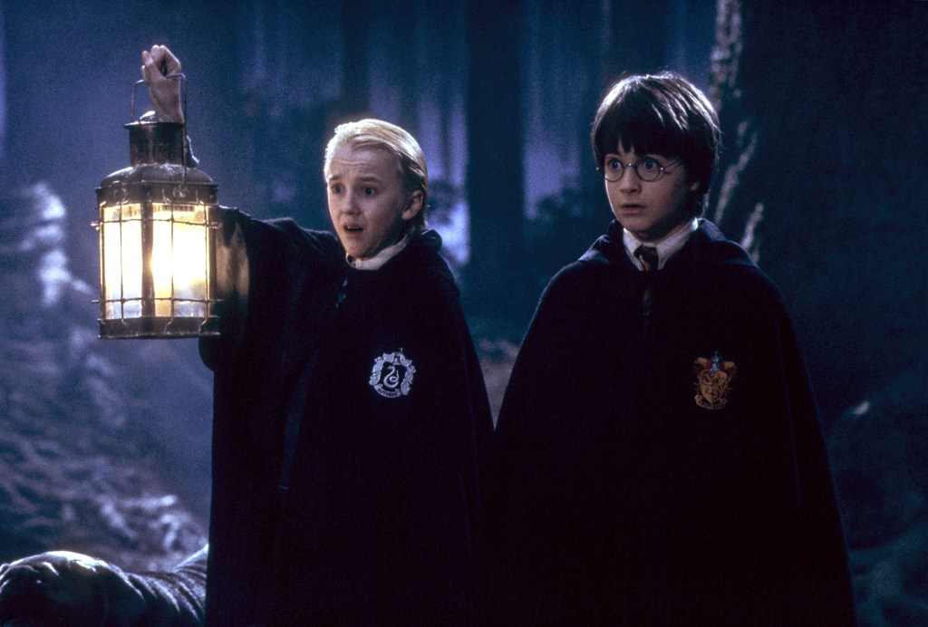 Draco Malfoy holding a lantern while Harry Potter looks on.