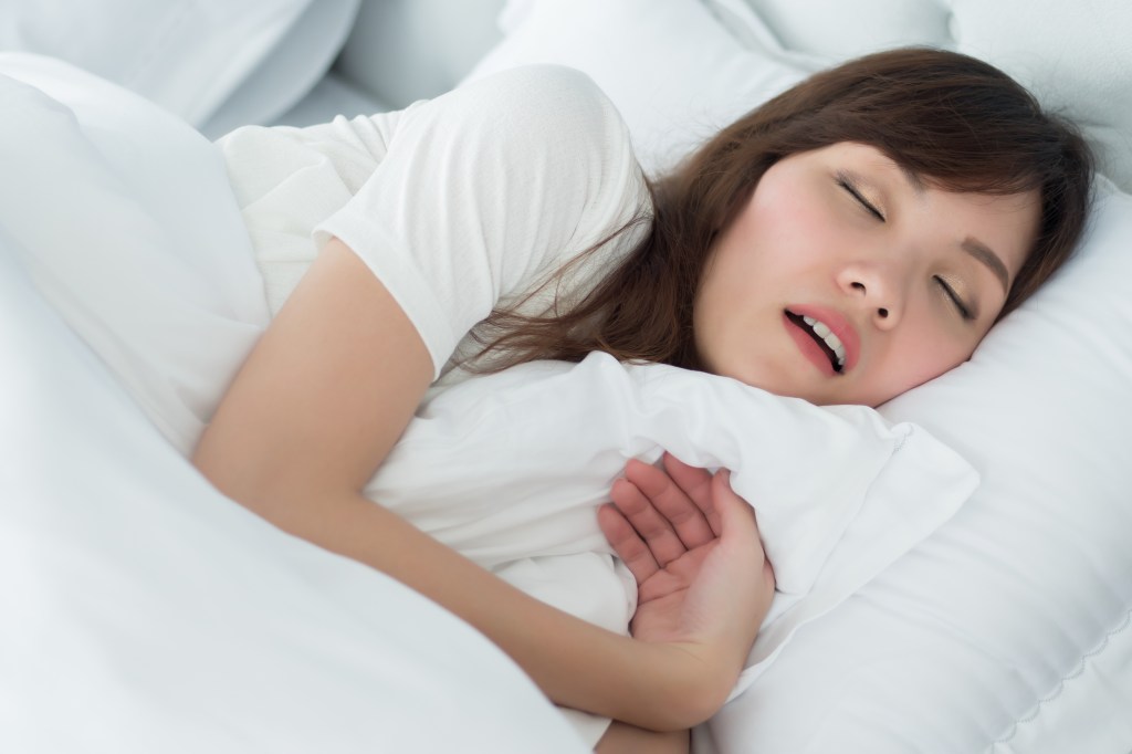 A sleeping Asian woman with her mouth open, snoring in bed.