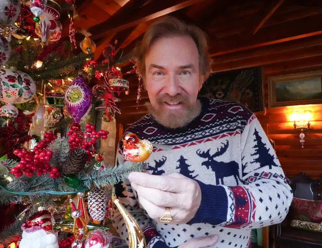 Ornament designer Christopher Radko holding a bird ornament on a decorated Christmas tree.