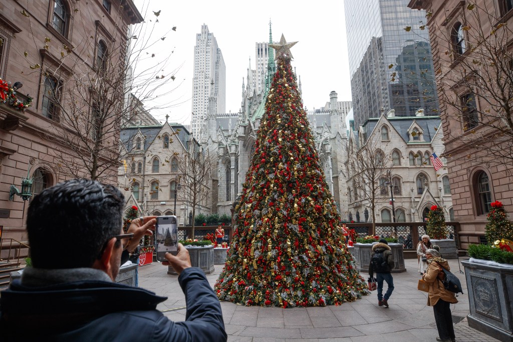 A person taking a photo of a large, decorated Christmas tree outside the Lotte New York Palace Hotel.