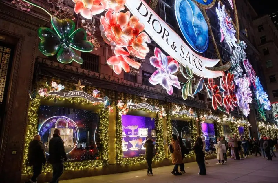 The facade of the Christian Dior and SAKS building decorated with large, colorful, glowing floral designs and a banner for a holiday-themed tour.