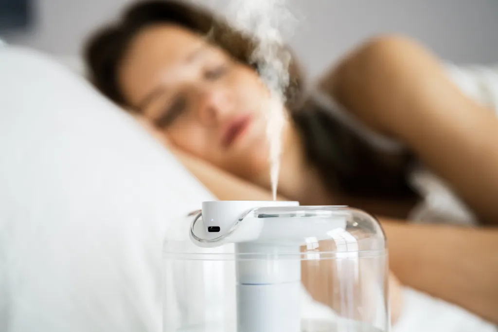Humidifier device in a bedroom with a sleeping woman in the background.