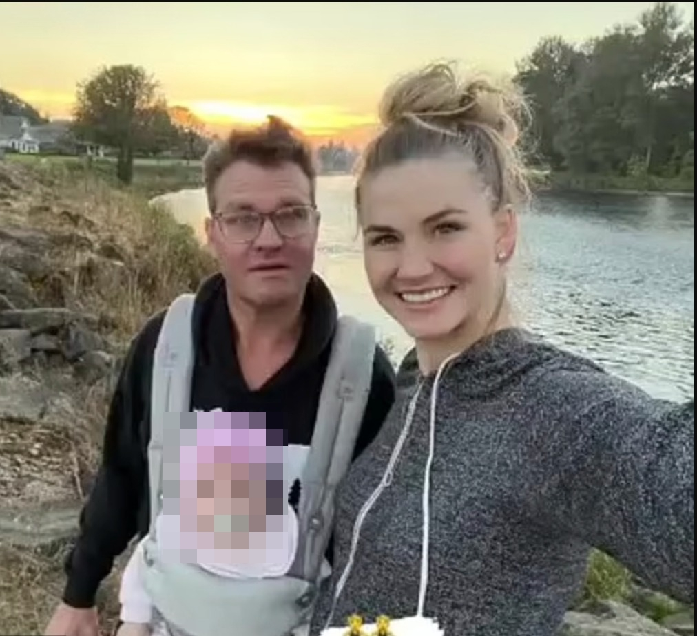 Zachery Ty Bryan, his girlfriend, and a blurred baby in a carrier pose by a river at sunset.