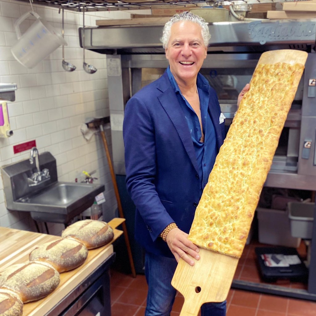 Serafina restaurant founder Vittorio Assaf holding a large focaccia bread.
