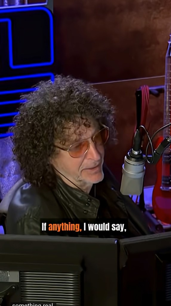 Howard Stern wearing sunglasses and a black leather jacket, with a microphone in front of him.