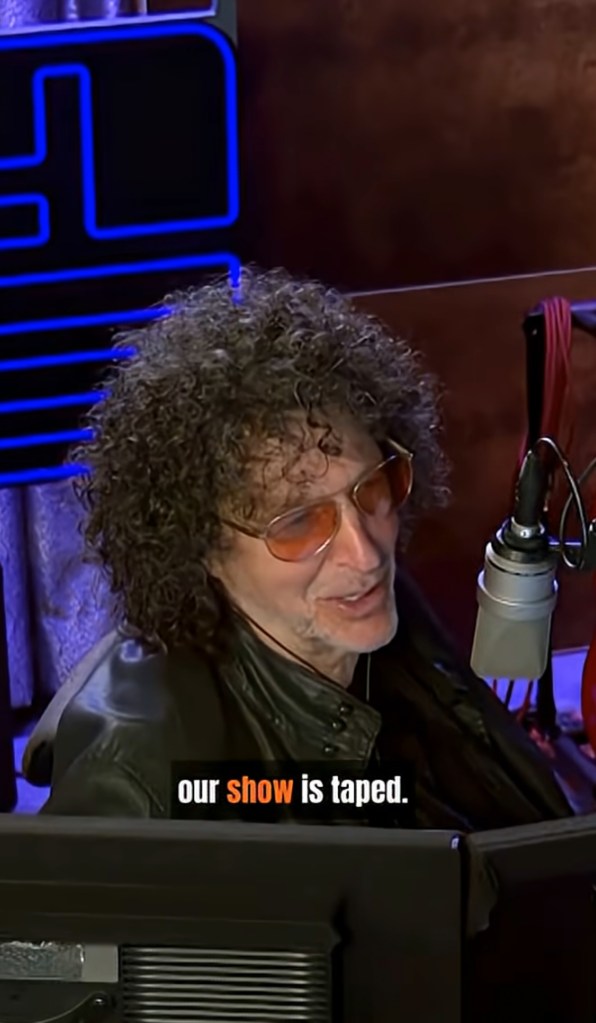 Howard Stern wearing a black leather jacket and orange-tinted sunglasses, speaking into a microphone.