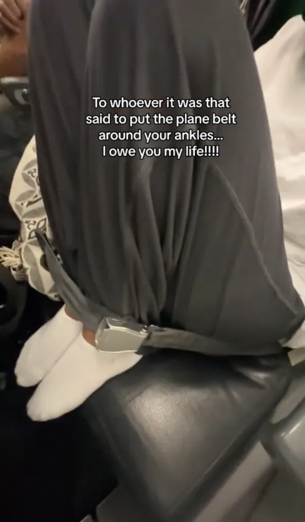 A person with their feet tucked onto the seat in front of them with the airplane seatbelt fastened around their ankles. Text reads 