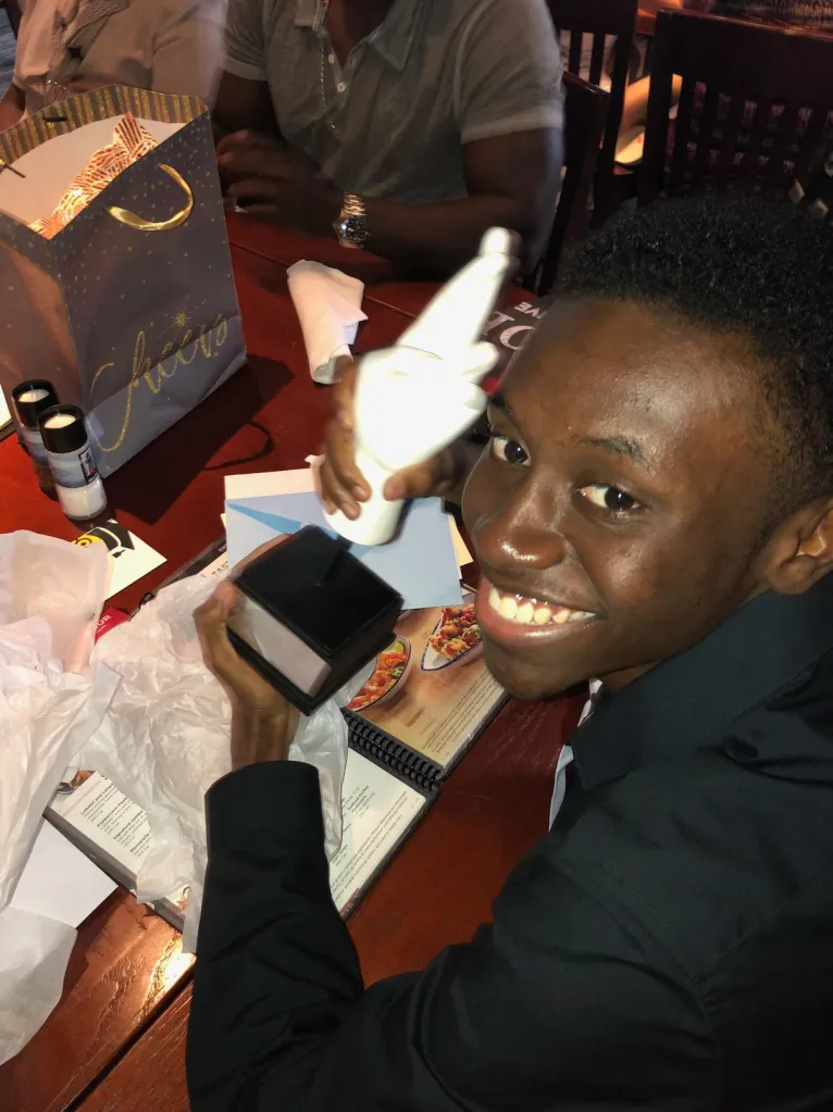 Donovan Metayer smiles at the camera while holding an opened gift box and a wrapped utensil.