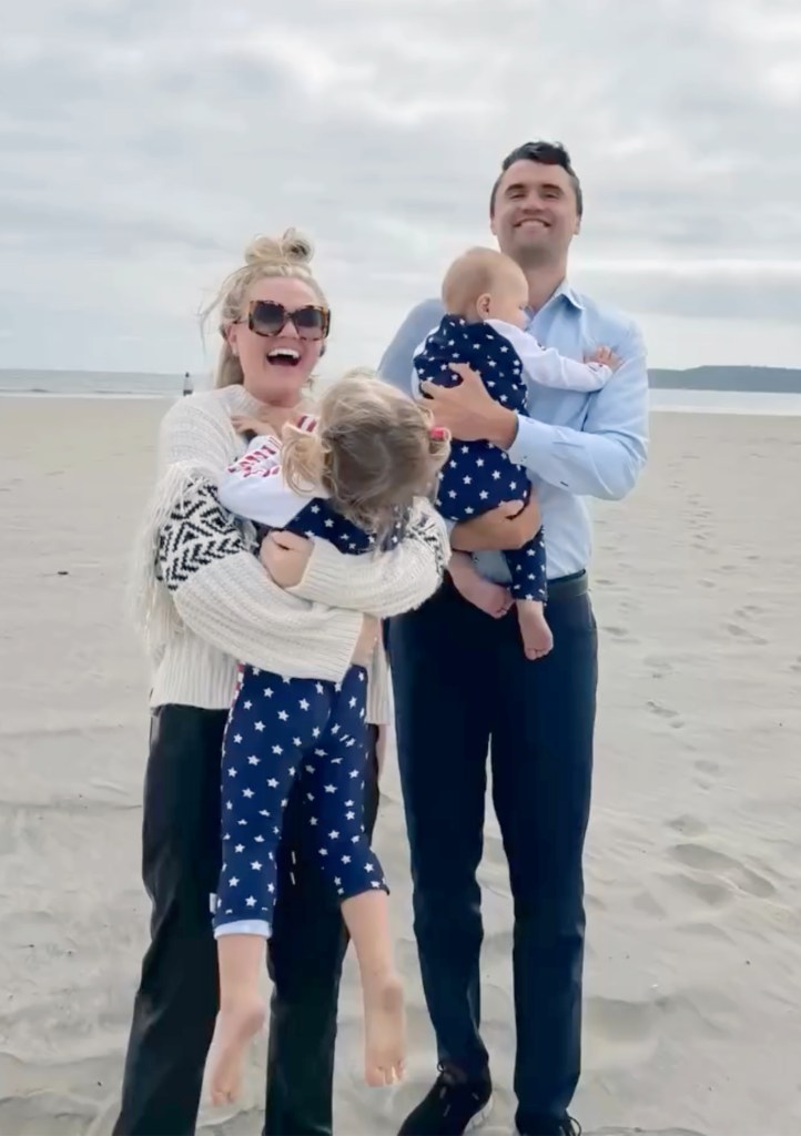 Charlie Kirk and his wife, Erika, each holding a child on a sandy beach.