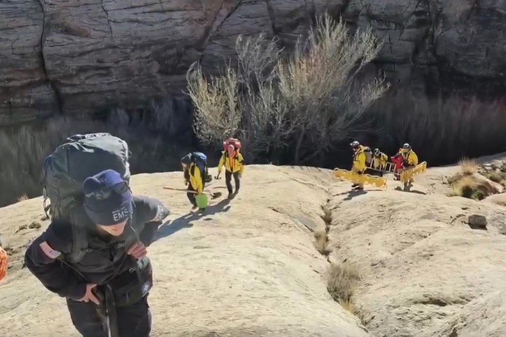 Emergency medical services (EMS) personnel and rescue workers carry equipment over rocky terrain for a quicksand rescue.