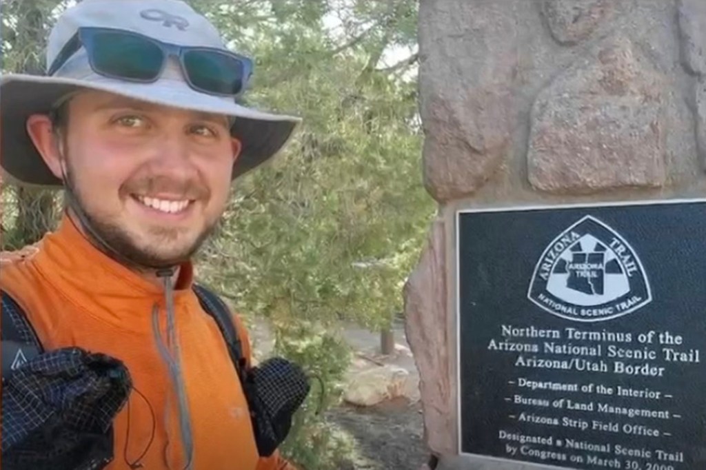 Austin Dirks smiling next to a sign for the Arizona National Scenic Trail.