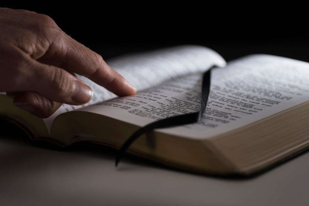 A human finger pointing to text on an open Bible.