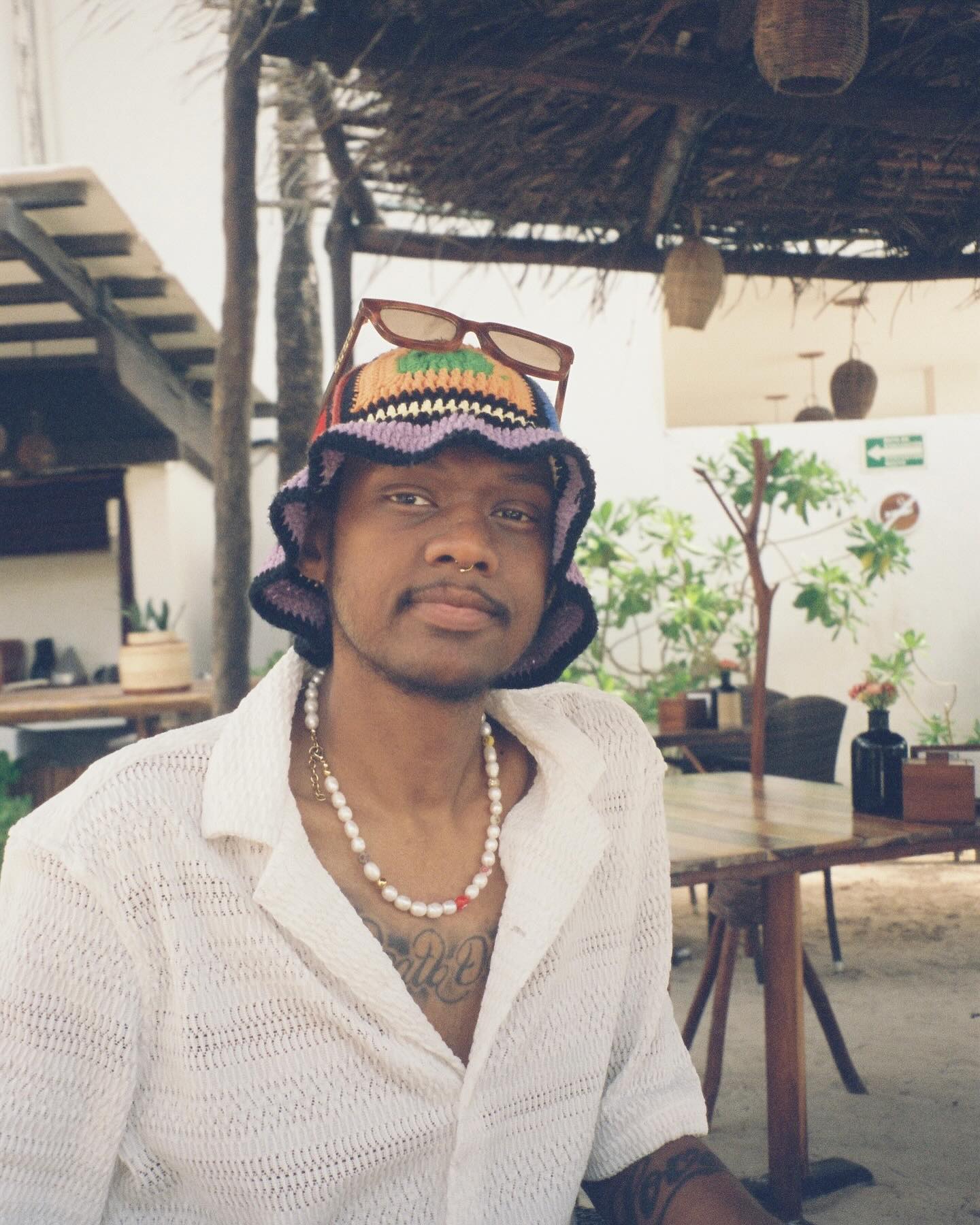 niko mcknight wearing a multi-colored crochet bucket hat, sunglasses on his head, and a pearl necklace.