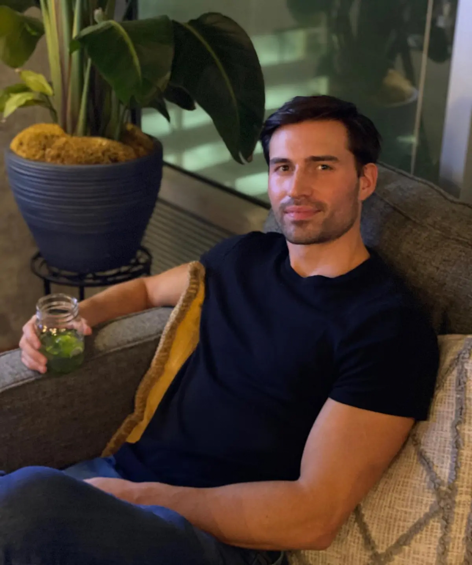 Actor Derek Dixon sits on a couch holding a drink.