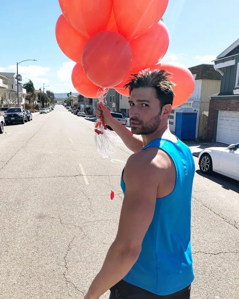 Derek Dixon holding a bunch of red balloons while standing in the middle of a street.