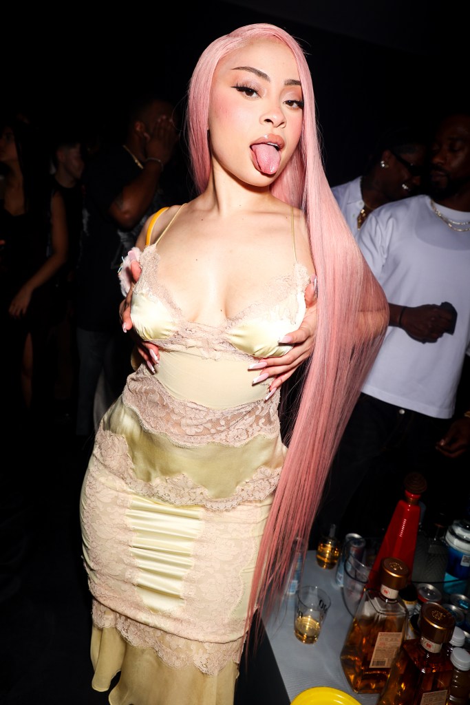 Ice Spice posing with pink hair and a light yellow dress with lace details.