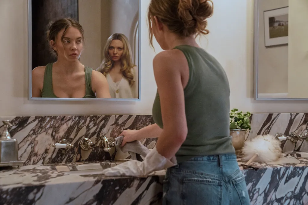 Sydney Sweeney looks into a mirror while Amanda Seyfried looks over her shoulder, in a scene from