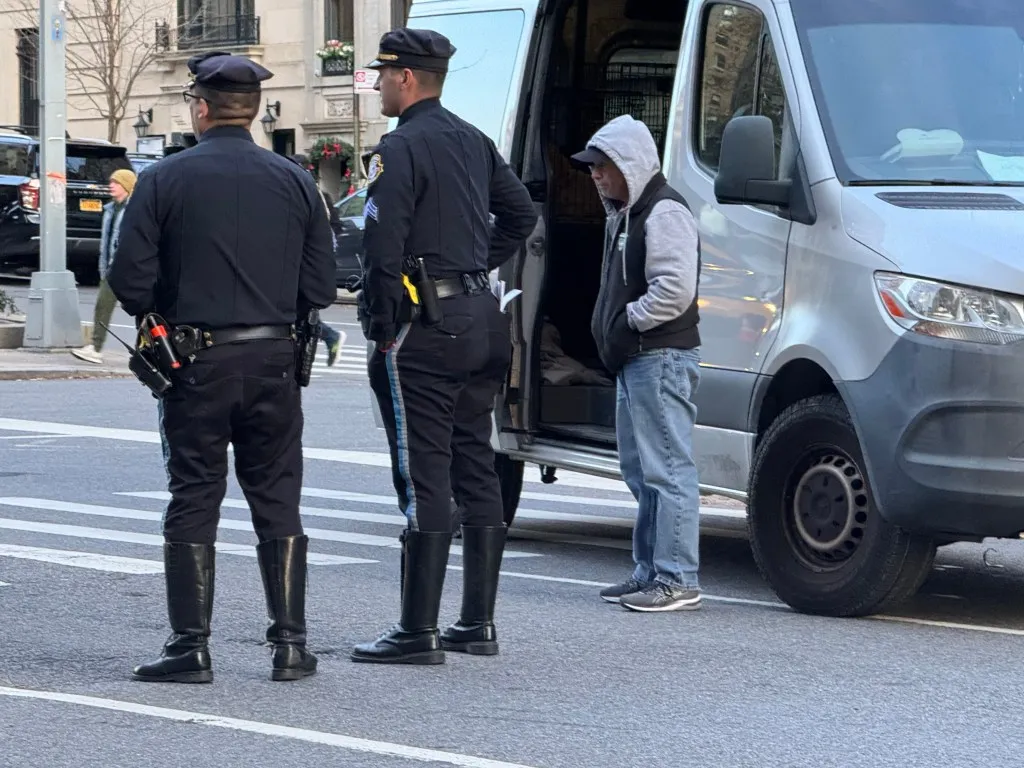 Two police officers and a civilian stand by a white van.