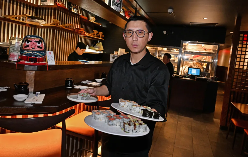 Server Robin Liu carrying plates of sushi at Imasa Nori Sushi Izakaya restaurant.