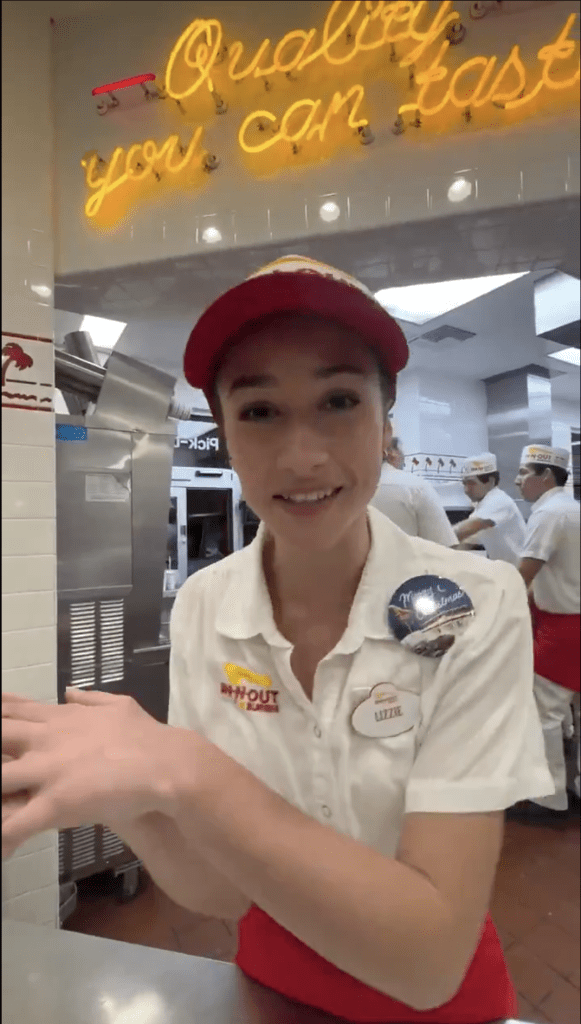 An In-N-Out employee, wearing a red hat and white uniform with a name tag
