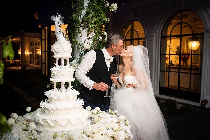 Gwen Stefani and Blake Shelton kissing next to their wedding cake.
