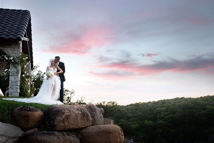 Gwen Stefani and Blake Shelton at their wedding, with a pink-tinged sky behind them.