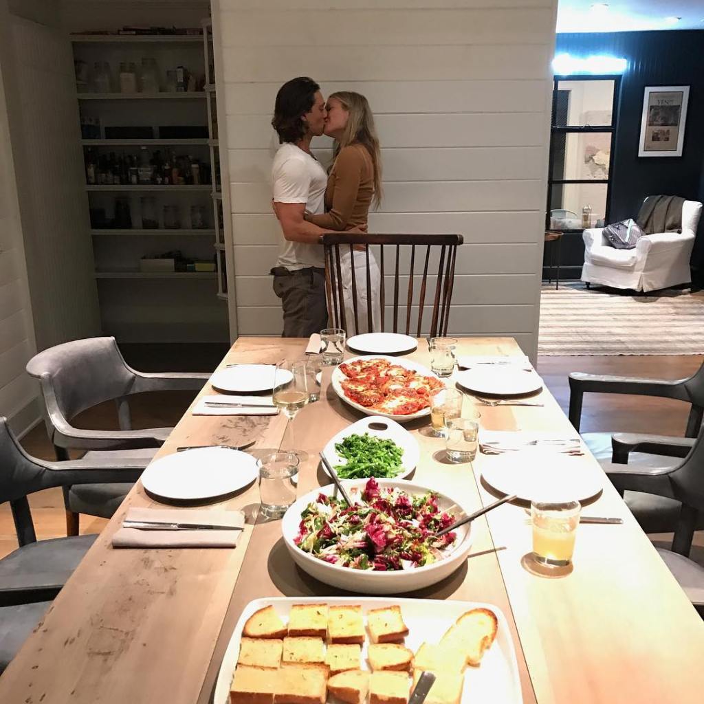 Gwyneth Paltrow and Brad Falchuk kissing, with a set dining table in the foreground.