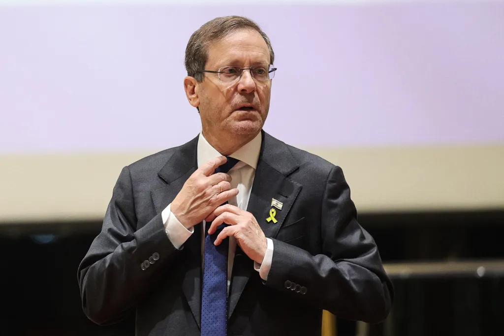 Israel's President Isaac Herzog adjusting his tie, wearing a yellow ribbon and Israeli flag pin.