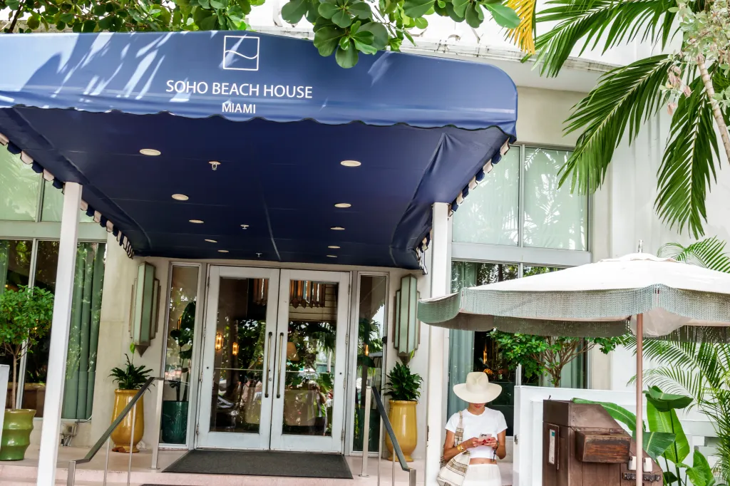 Soho Beach House Miami awning sign on Collins Avenue, with a woman texting on her phone.