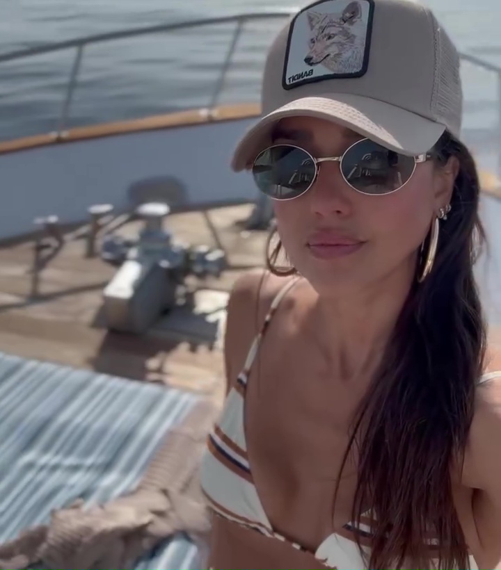 Jessica Alba in a white striped bikini, wearing a baseball cap and sunglasses on a yacht.