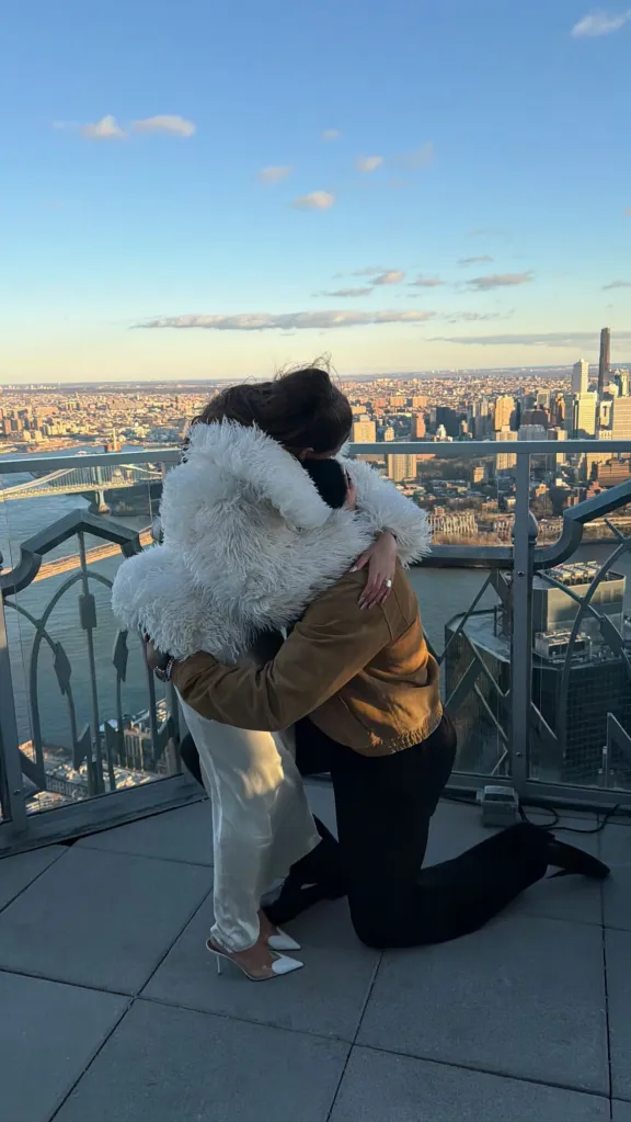 Jordyn Woods embracing a person kneeling on a rooftop overlooking a city.