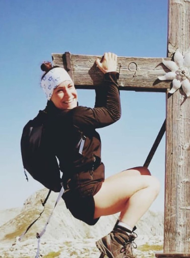 Kerstin Gurtner hanging from a wooden cross with an edelweiss emblem.