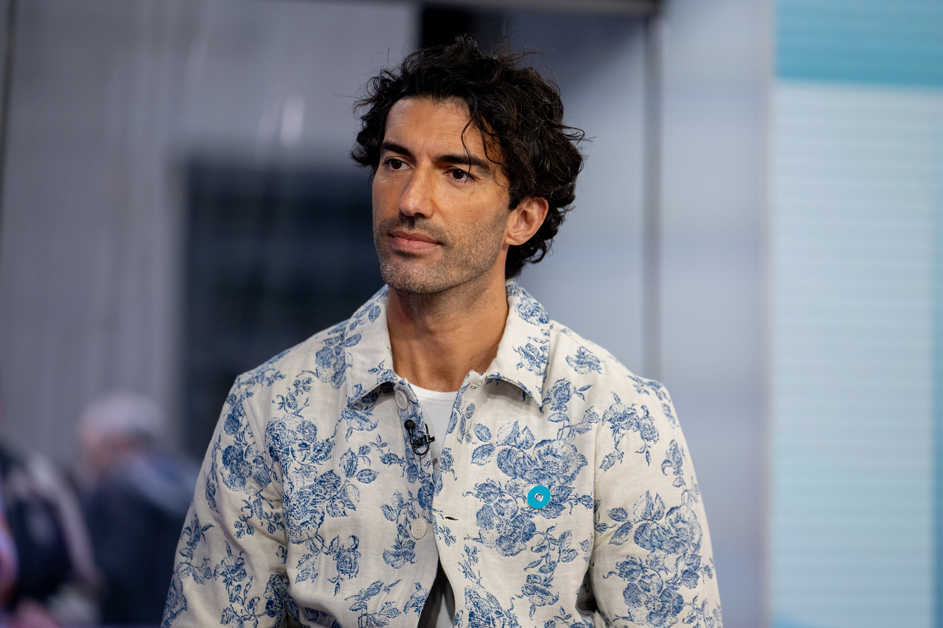 Justin Baldoni wearing a blue floral print jacket with a light blue pin on the lapel.