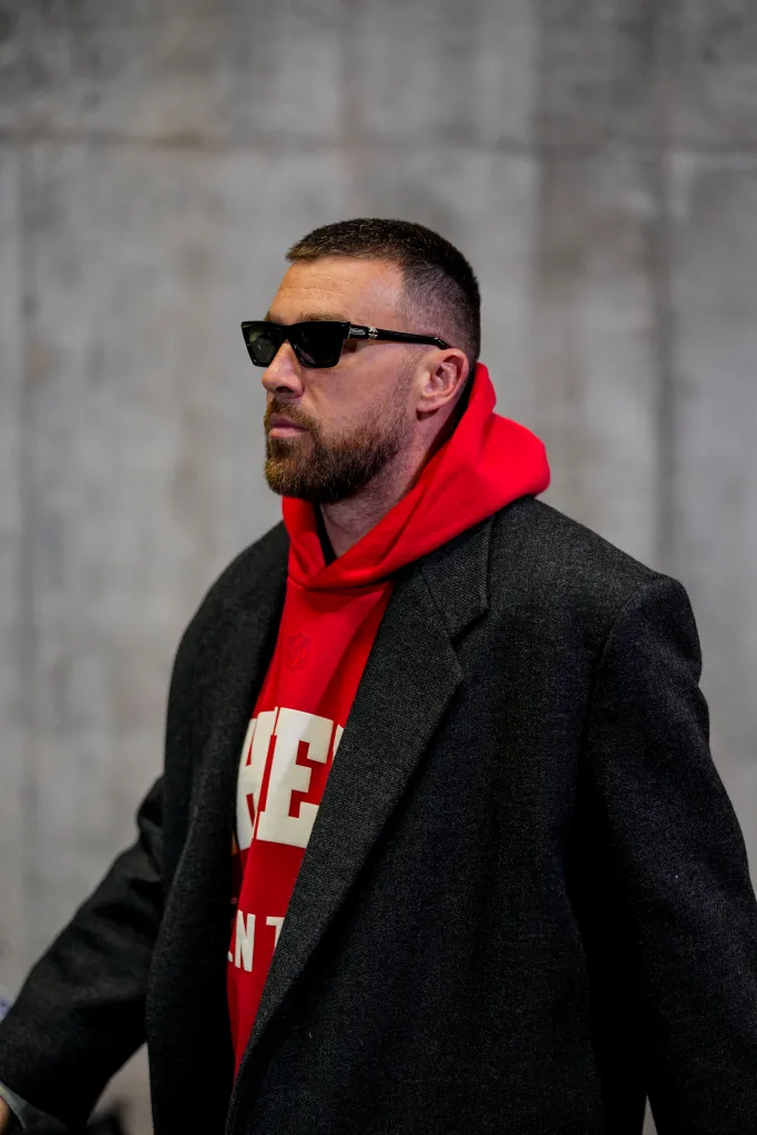 Kansas City Chiefs tight end Travis Kelce wearing sunglasses and a red Chiefs hoodie with a gray coat.