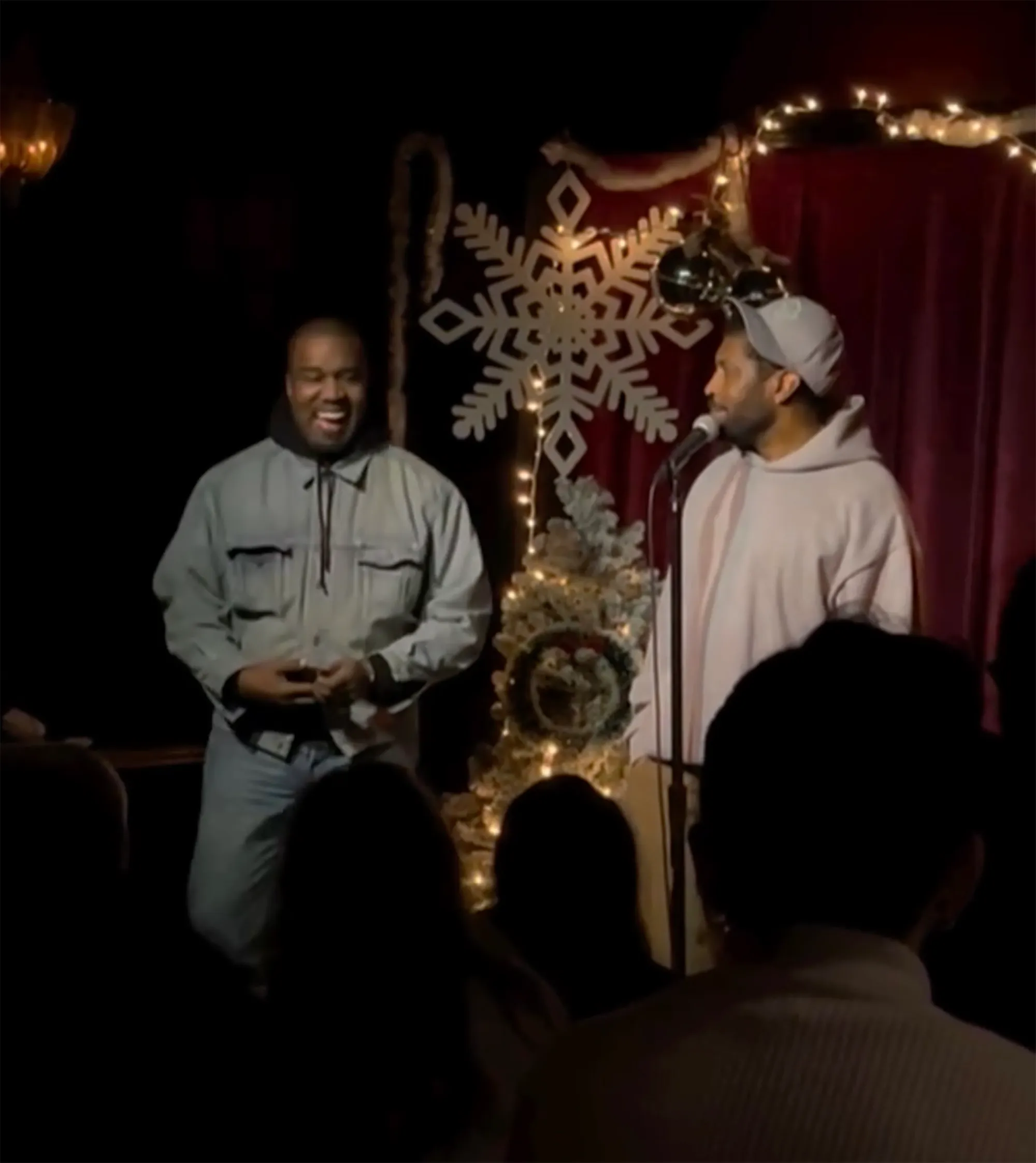 Deon Cole at a microphone with Kanye West laughing beside him.