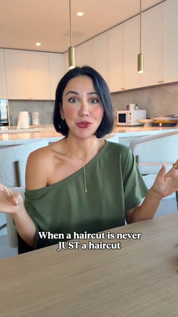 Kat Stickler, with a bob haircut and a green off-shoulder top, sits at a table and appears to be speaking to the camera.