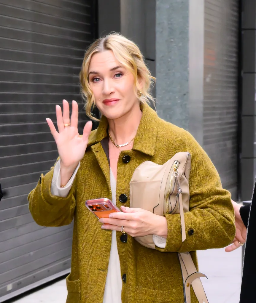 Kate Winslet waving and holding her phone.