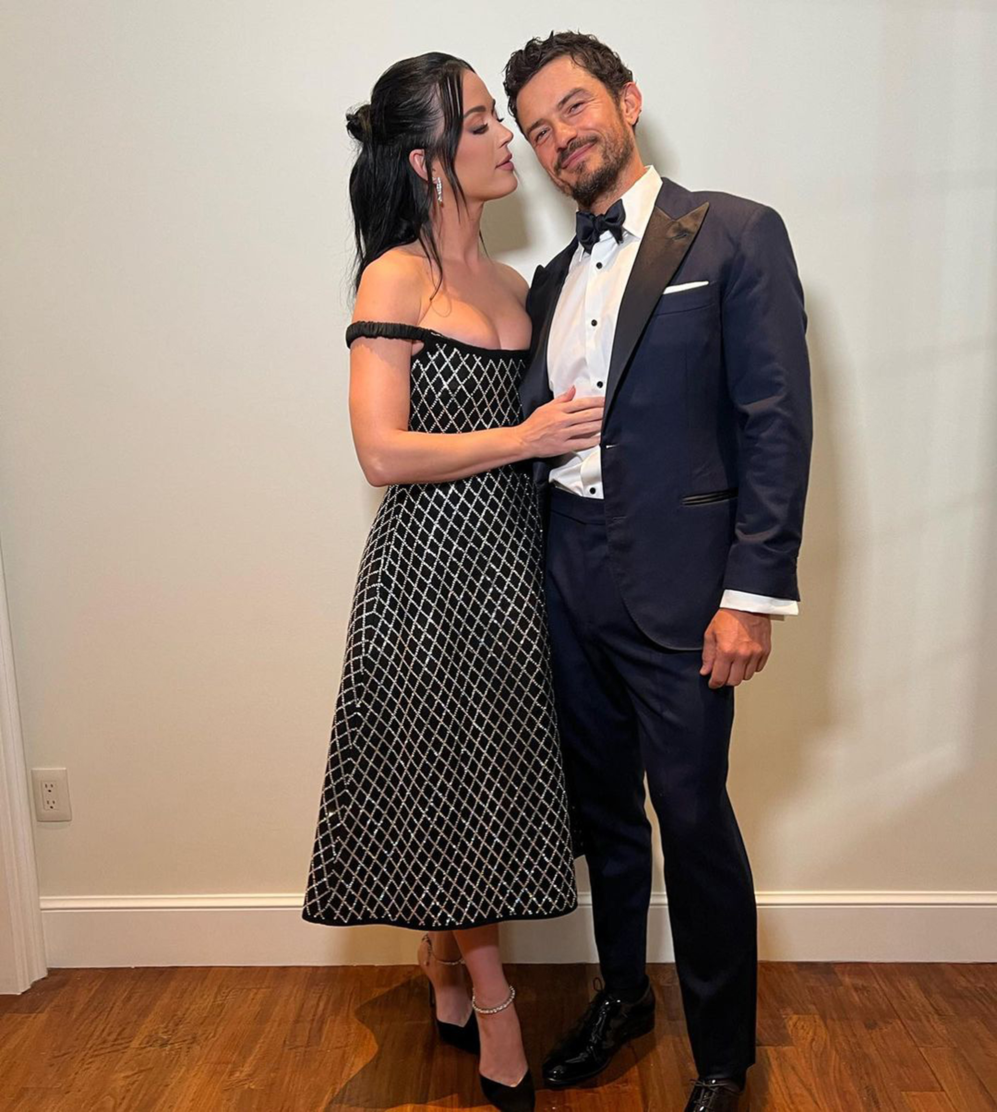 Katy Perry in a black and silver dress leaning into Orlando Bloom in a tuxedo.