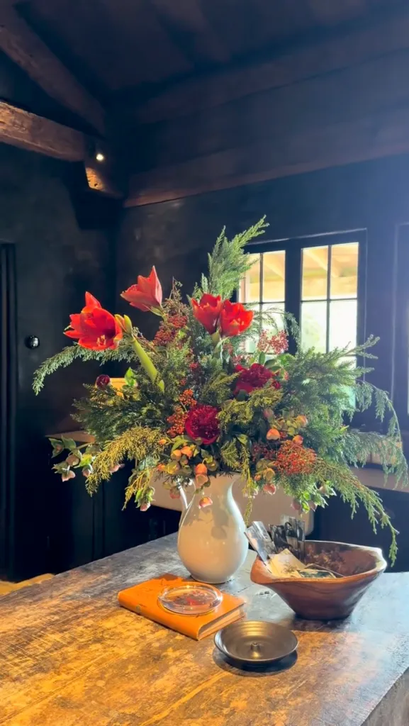A festive floral arrangement with red flowers and greenery on a wooden table.