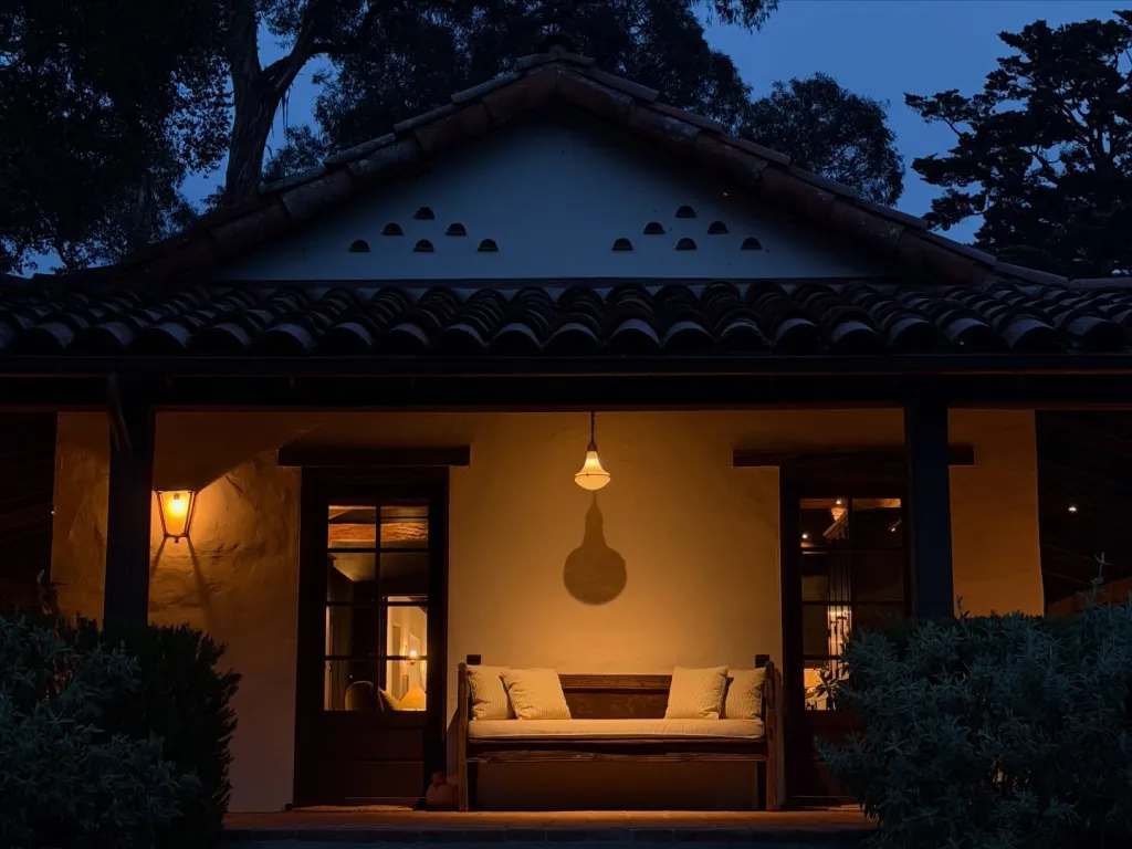 A house with a lit porch and bench at dusk.