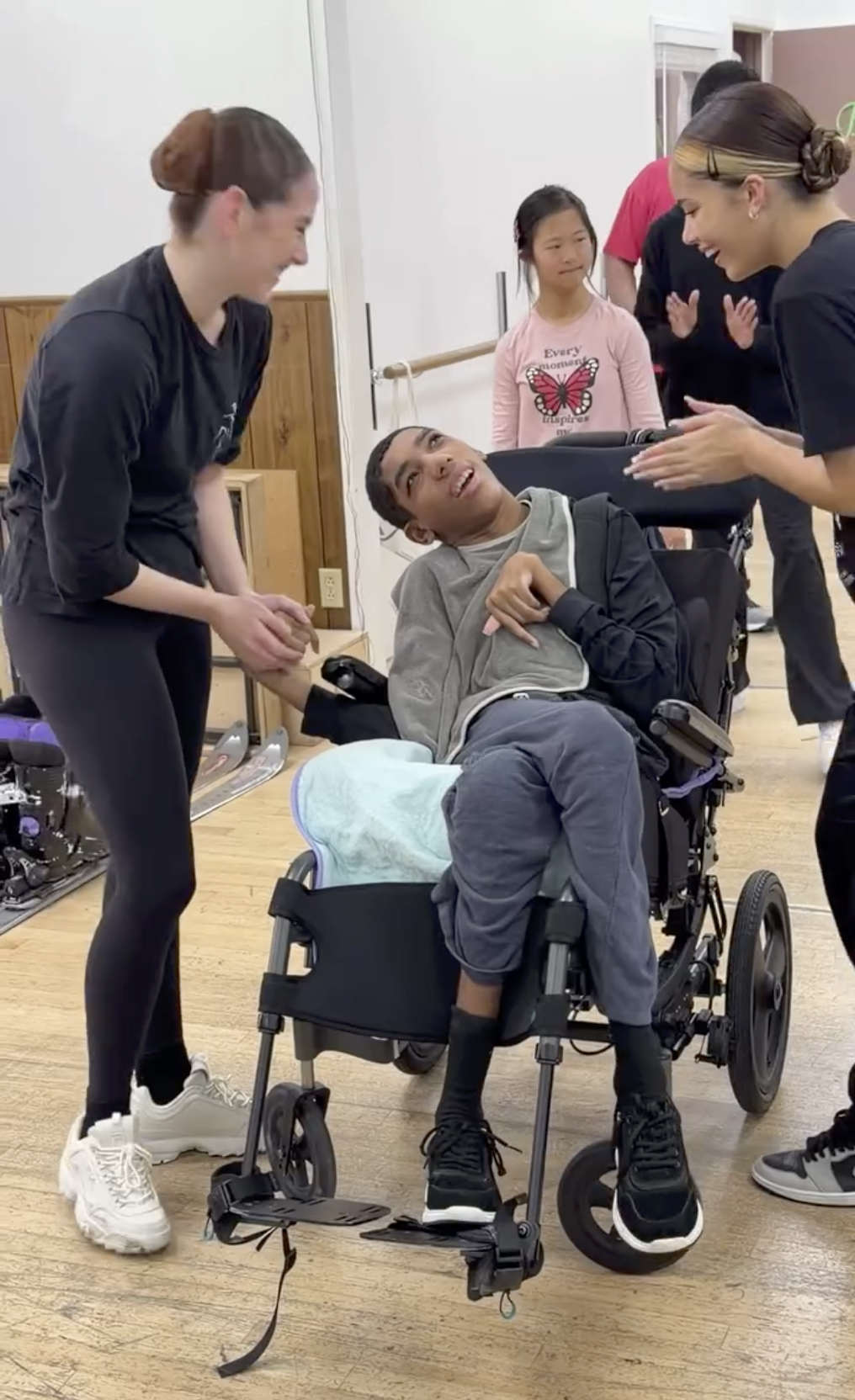 Amari Thompson in a wheelchair at dance class, with two women standing beside him.