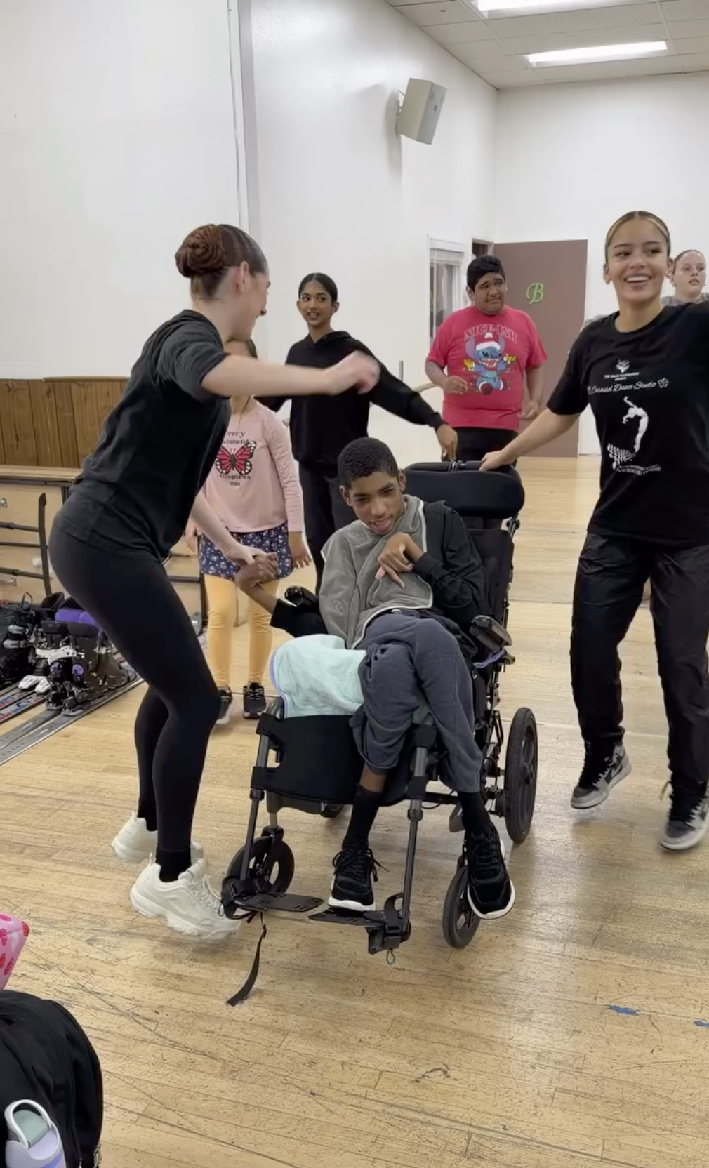 Amari Thompson in a specialized power wheelchair smiling while dance instructors spin them around.