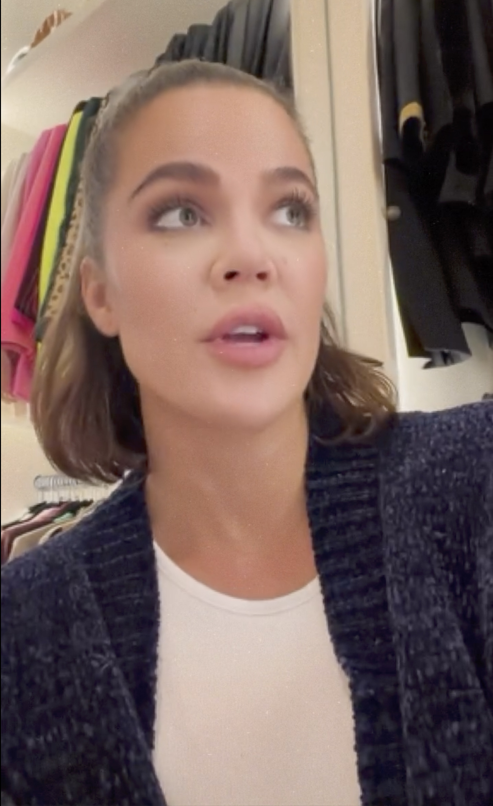 Khloé Kardashian in a navy blue cardigan over a white shirt, speaking directly to the camera.